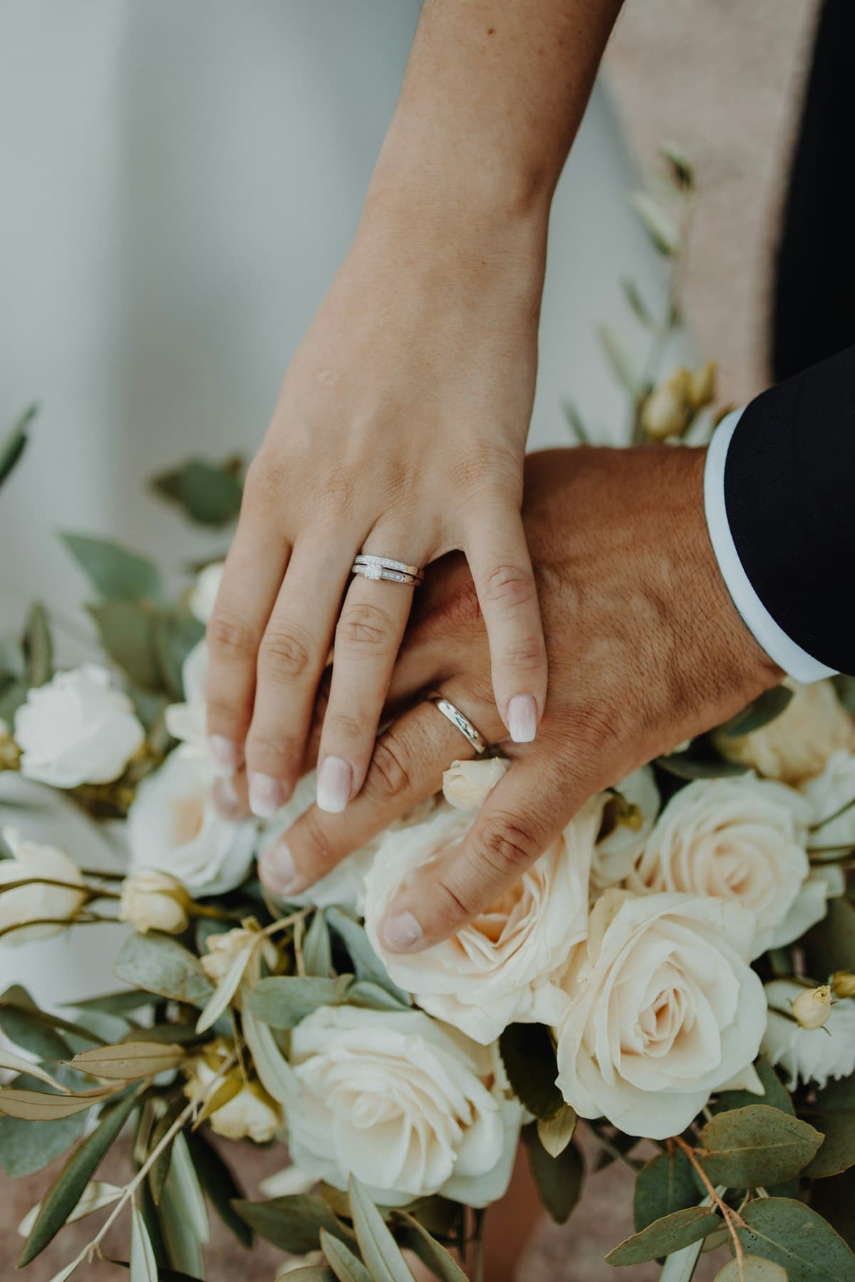 Las manos de los novios, con sus alianzas, sobre un ramo de rosas blancas.
