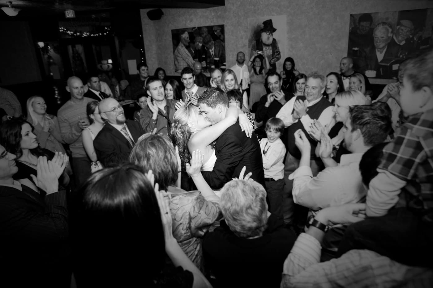 Los novios se abrazan en medio de los invitados que aplauden, en blanco y negro.