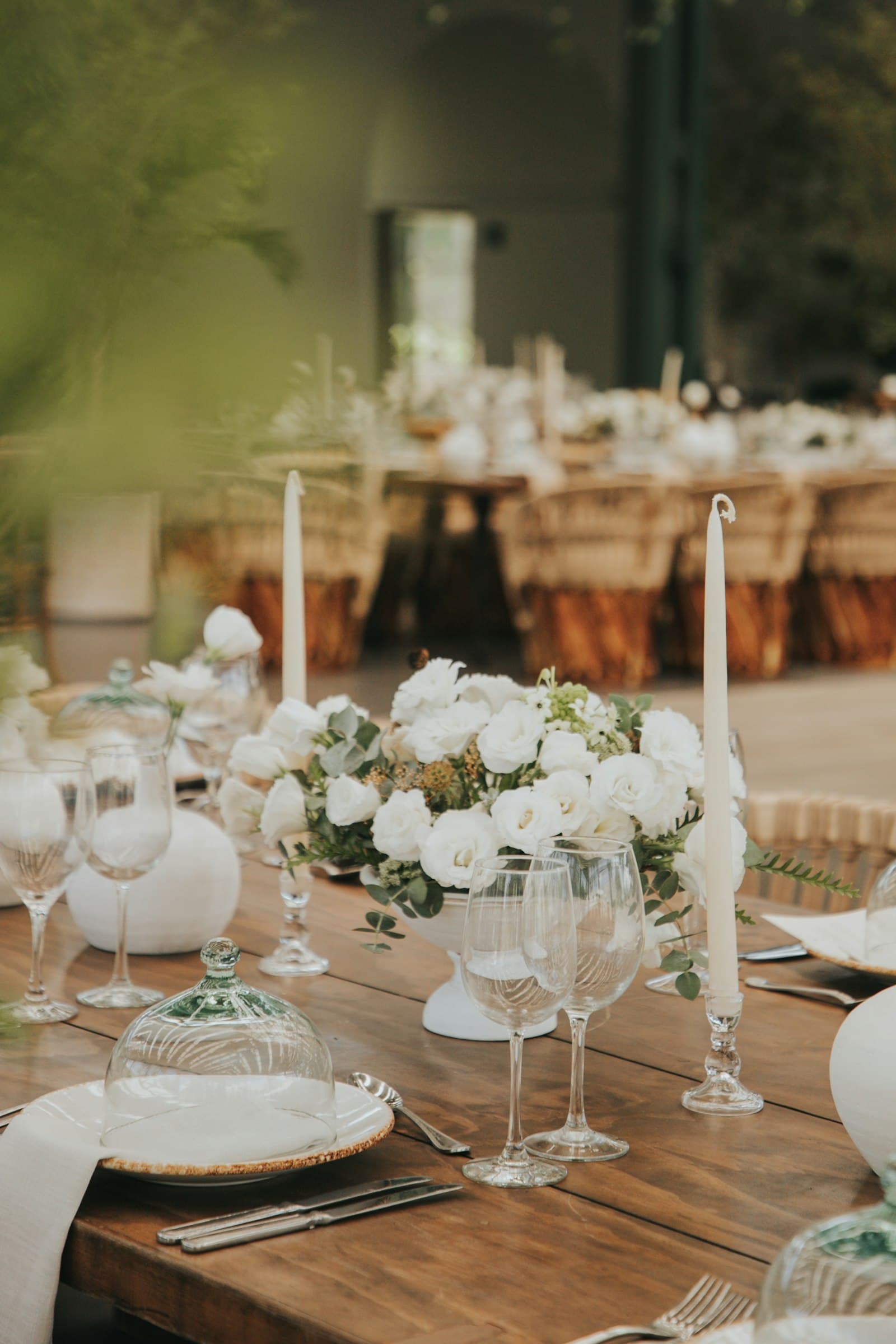 Una mesa de madera puesta con velas altas, copas y flores blancas.