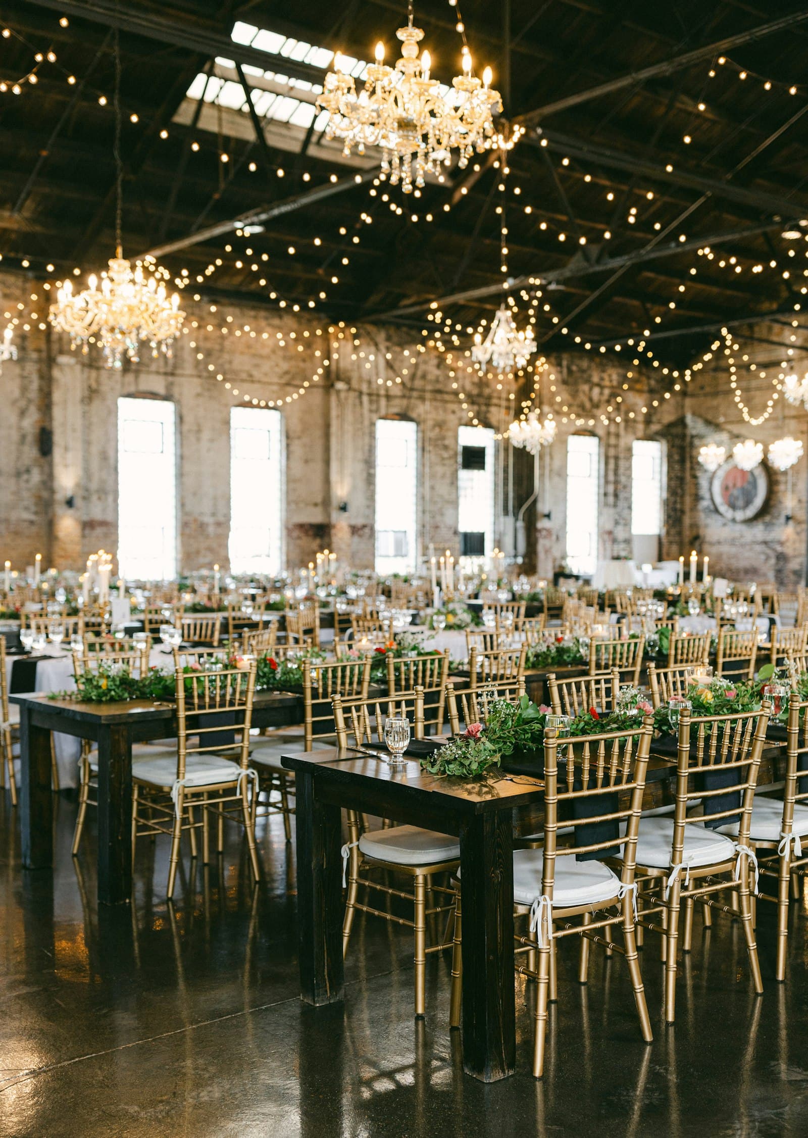 Un salón con arañas de cristal y guirnaldas de luces, con las mesas listas antes de la fiesta.